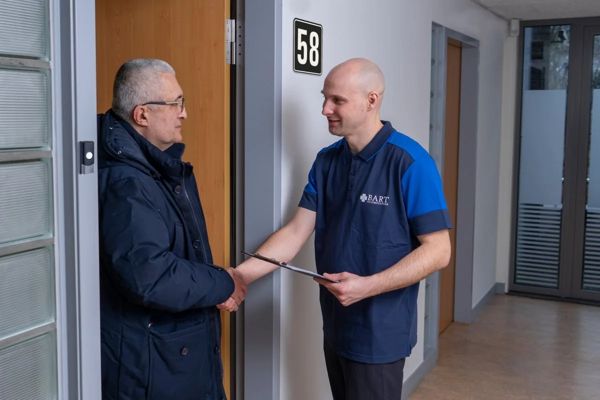Huismeester geeft een bewoner een hand bij de voordeur
